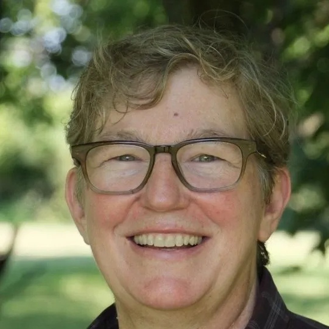 Lora Covrett smiling outdoors in a plaid shirt and glasses