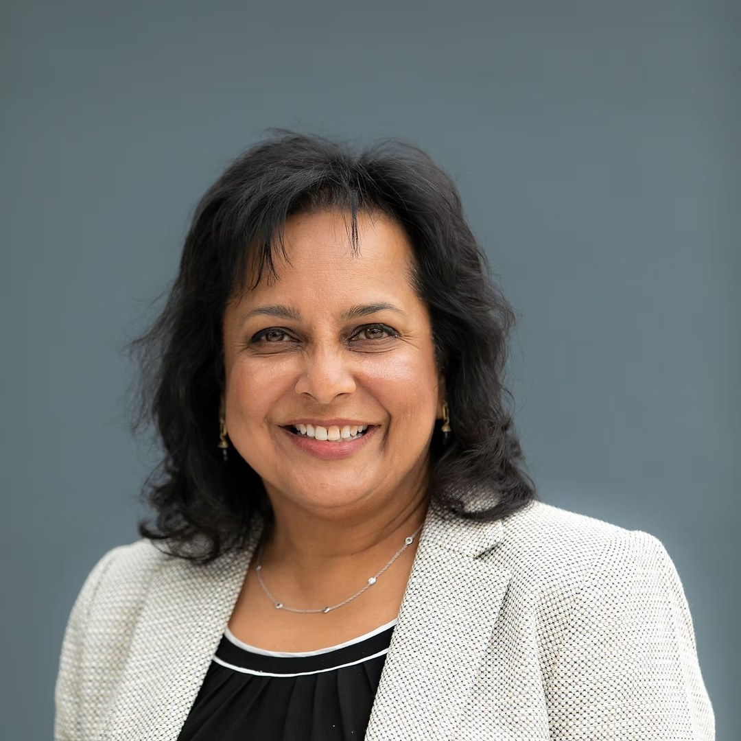 Manisha Kotian smiling in a cream blazer over a black top