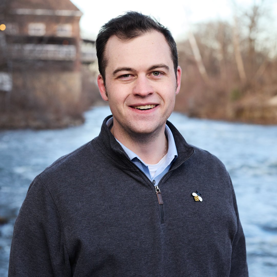 J. Noah Spinner smiling in a charcoal quarter-zip beside the Cuyahoga River in Cuyahoga Falls